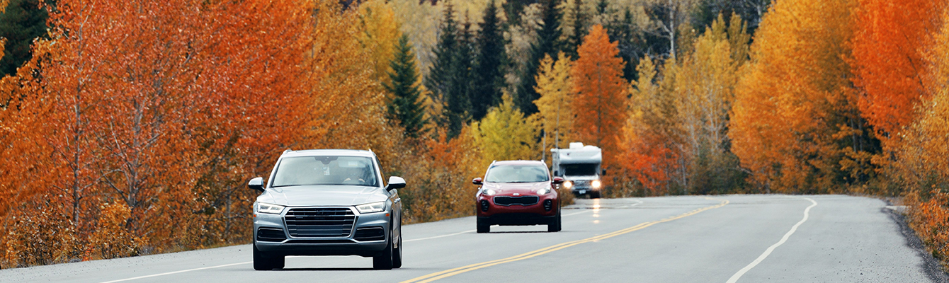 Three vehicles using Esso fuels drive down a Canadian highway with changing fall leaves in view.