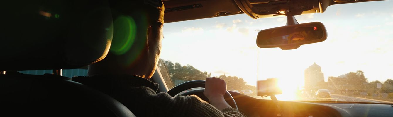 Person driving a car using our unleaded fuel with sunset shining through front windshield
